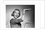 1950s 1960s happy smiling blond woman gesturing with hands showing size of something looking at camera by Anonymous