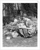 1930s 1940s woman dressed in print dress striped apron kneeling in flowers garden reading a gardening manual by Anonymous