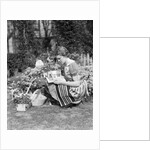 1930s 1940s woman dressed in print dress striped apron kneeling in flowers garden reading a gardening manual by Anonymous