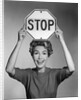 1950s 1960s smiling woman holding stop sign above her head looking at camera by Anonymous