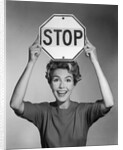 1950s 1960s smiling woman holding stop sign above her head looking at camera by Anonymous