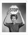 1950s 1960s smiling woman holding stop sign above her head looking at camera by Anonymous