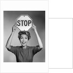 1950s 1960s smiling woman holding stop sign above her head looking at camera by Anonymous