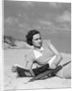 1930s woman leaning in wooden chair on beach wearing printed dress holding magazine looking thoughtful by Anonymous