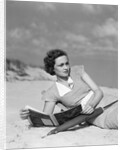 1930s woman leaning in wooden chair on beach wearing printed dress holding magazine looking thoughtful by Anonymous