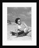 1930s woman leaning in wooden chair on beach wearing printed dress holding magazine looking thoughtful by Anonymous