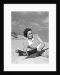 1930s woman leaning in wooden chair on beach wearing printed dress holding magazine looking thoughtful by Anonymous