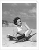 1930s woman leaning in wooden chair on beach wearing printed dress holding magazine looking thoughtful by Anonymous