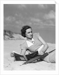 1930s woman leaning in wooden chair on beach wearing printed dress holding magazine looking thoughtful by Anonymous