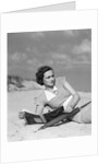 1930s woman leaning in wooden chair on beach wearing printed dress holding magazine looking thoughtful by Anonymous