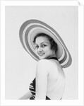 1930s woman wearing striped halter top and very wide brim straw hat looking at camera over shoulder by Anonymous