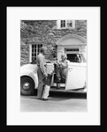 1940s senior retired couple loading golf clubs into white convertible car in front stone house by Anonymous