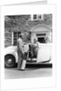 1940s senior retired couple loading golf clubs into white convertible car in front stone house by Anonymous