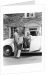 1940s senior retired couple loading golf clubs into white convertible car in front stone house by Anonymous