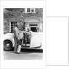 1940s senior retired couple loading golf clubs into white convertible car in front stone house by Anonymous