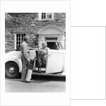1940s senior retired couple loading golf clubs into white convertible car in front stone house by Anonymous