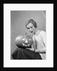 1950s woman wearing sweater holding carved pumpkin jack-o-lantern on her lap by Anonymous