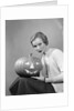1950s woman wearing sweater holding carved pumpkin jack-o-lantern on her lap by Anonymous
