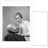1950s woman wearing sweater holding carved pumpkin jack-o-lantern on her lap by Anonymous