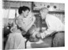 1950s housewife in kitchen having husband taste food on stove by Anonymous
