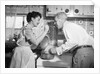 1950s housewife in kitchen having husband taste food on stove by Anonymous