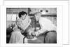 1950s housewife in kitchen having husband taste food on stove by Anonymous