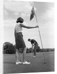 1970s couple playing golf man putting woman holding flag by Anonymous