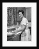 1960s woman housewife washing dishes in kitchen sink looking at camera by Anonymous