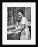 1960s woman housewife washing dishes in kitchen sink looking at camera by Anonymous