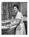 1960s woman housewife washing dishes in kitchen sink looking at camera by Anonymous