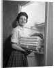 1950s 1960s housewife holding laundry folded towels by linen closet looking at camera by Anonymous