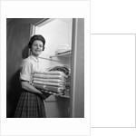 1950s 1960s housewife holding laundry folded towels by linen closet looking at camera by Anonymous