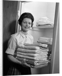 1960s woman holding laundry folded towels by linen closet looking at camera by Anonymous