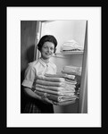 1960s woman holding laundry folded towels by linen closet looking at camera by Anonymous