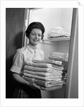 1960s woman holding laundry folded towels by linen closet looking at camera by Anonymous