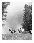 1950s 1960s two men on horseback riding across field wearing cowboy hats by Anonymous