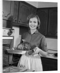 1960s smiling woman in kitchen taking roast out of oven looking at camera by Anonymous