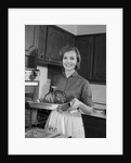 1960s smiling woman in kitchen taking roast out of oven looking at camera by Anonymous