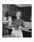 1960s smiling woman in kitchen taking roast out of oven looking at camera by Anonymous