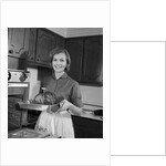 1960s smiling woman in kitchen taking roast out of oven looking at camera by Anonymous