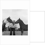 1960s boy wearing cowboy hat holding ropes reins harness halter of 2 horses one on either side of his face kissing him funny by Anonymous