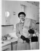 1950s smiling woman in kitchen holding grocery bag handbag wearing hat gloves looking at camera by Anonymous