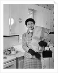 1950s smiling woman in kitchen holding grocery bag handbag wearing hat gloves looking at camera by Anonymous