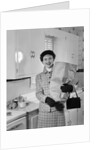 1950s smiling woman in kitchen holding grocery bag handbag wearing hat gloves looking at camera by Anonymous