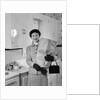 1950s smiling woman in kitchen holding grocery bag handbag wearing hat gloves looking at camera by Anonymous