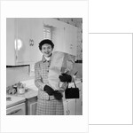 1950s smiling woman in kitchen holding grocery bag handbag wearing hat gloves looking at camera by Anonymous