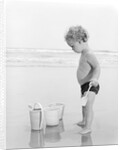 1960s 1970s child toddler standing in sand water bucket shovel by Anonymous