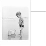 1960s 1970s child toddler standing in sand water bucket shovel by Anonymous