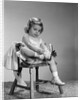 1960s little girl putting on shoes sitting on chair by Anonymous