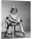 1960s little girl putting on shoes sitting on chair by Anonymous